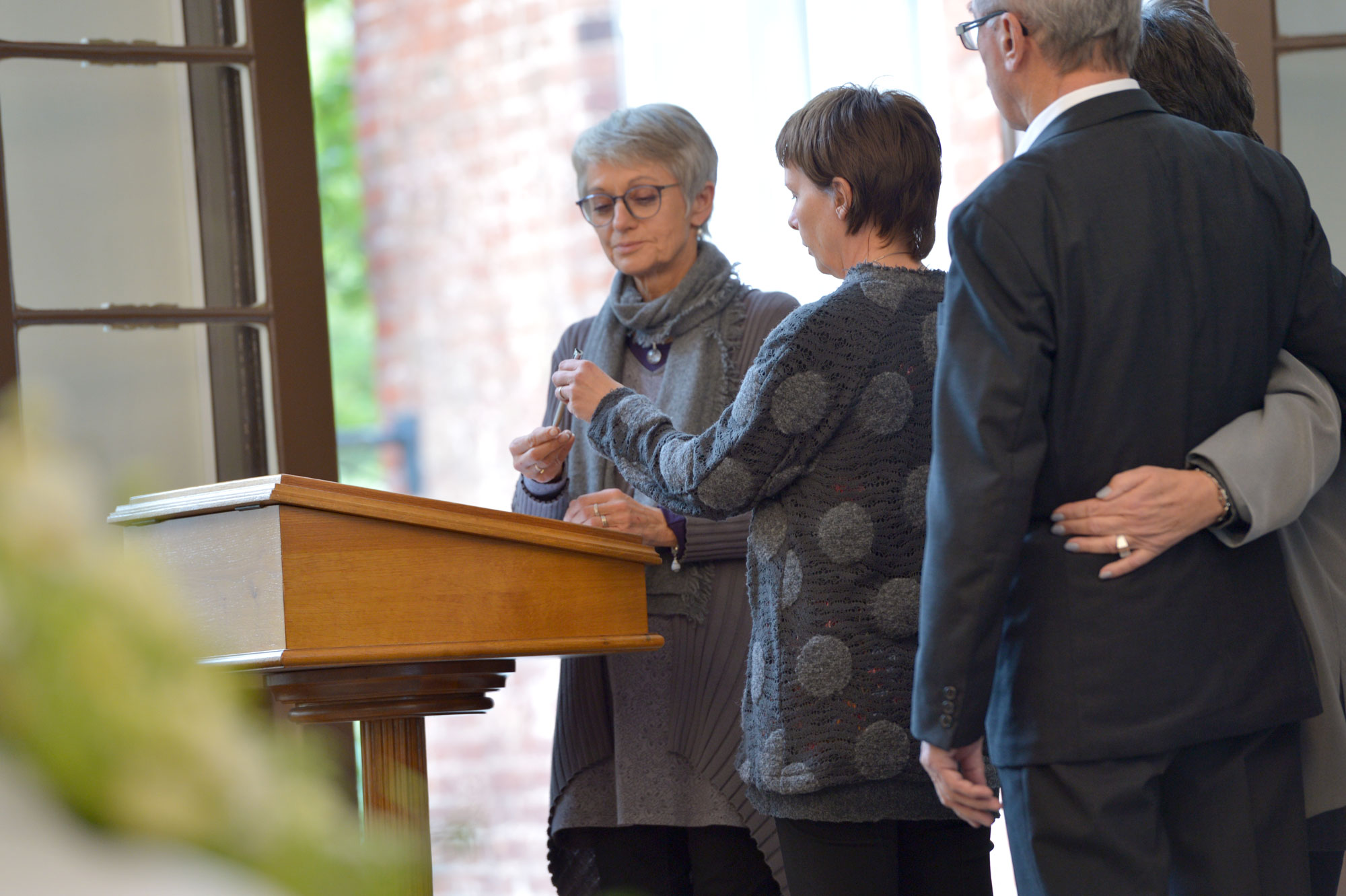 Eine Trauergemeinde steht Arm in Arm an einem Rednerpult. Eine Person hält eine Trauerrede.